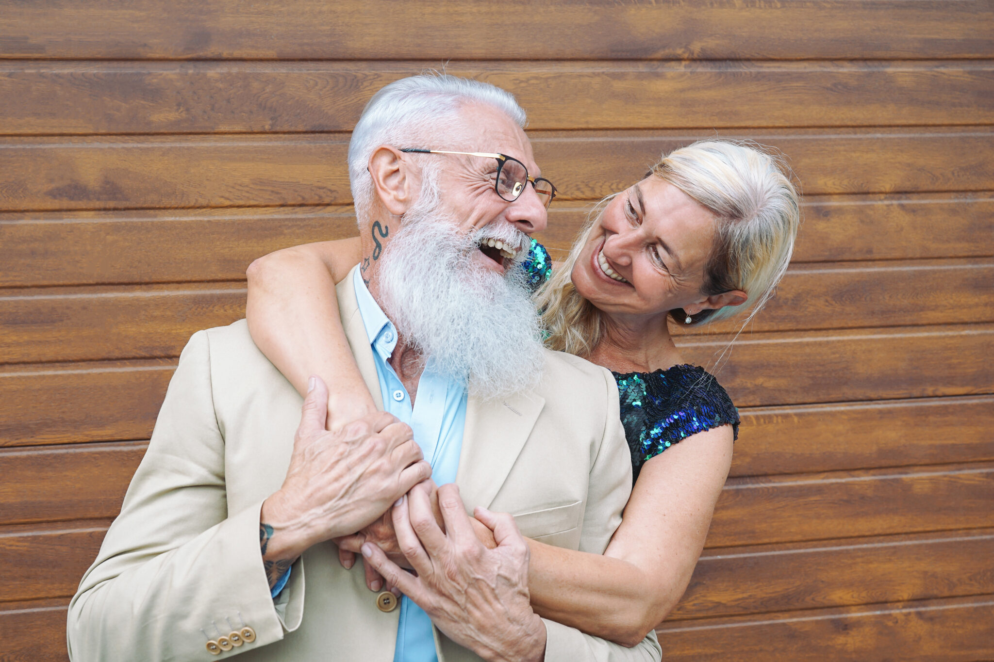 Happy fashion seniors couple embracing outdoor - Mature elegant people laughing and having a tender moment together - Concept of happiness, pensioners, love and relationship - Wooden background
