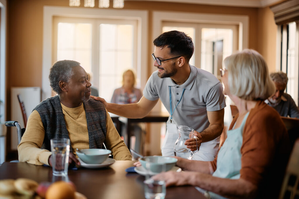 Assisted Living for Seniors with No Money: Young healthcare worker talking to seniors during lunch at nursing home.