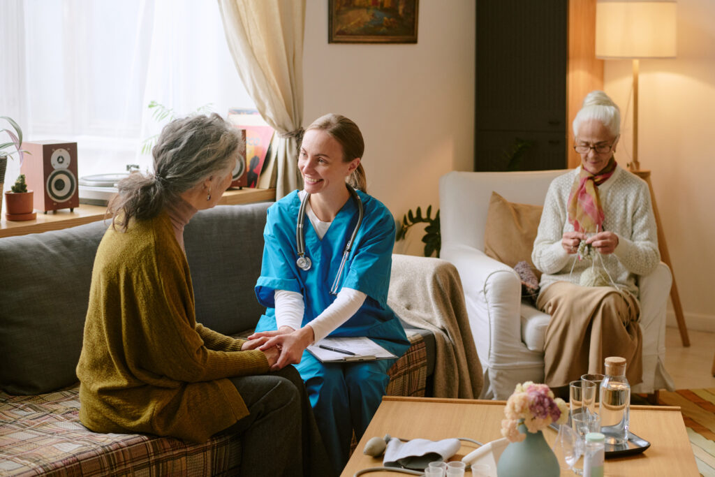 Assisted Living Room Ideas: Wide shot of young nurse holding hands of senior resident of nursing home while supporting her