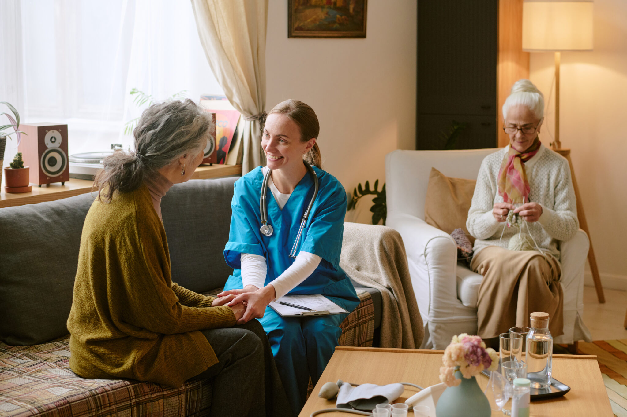 Wide shot of young nurse holding hands of senior resident of nursing home while supporting her