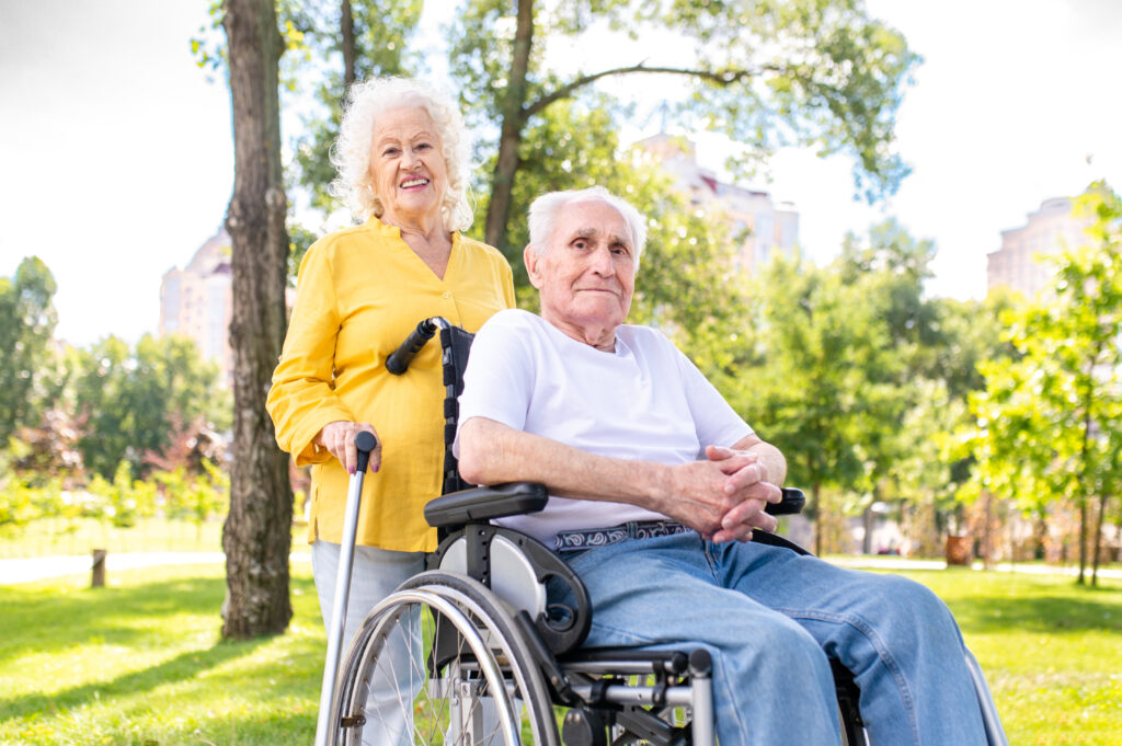 Beautiful senior couple with disability outdoors - Old people in the age of 60, 70, 80 having fun and spending time together, concepts about elderly, seniority, healthcare and wellness aging