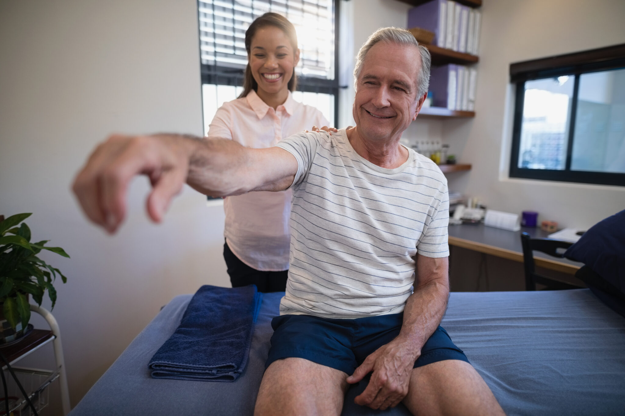 Smiling female doctor examining shoulder of senior male patient at hospital ward