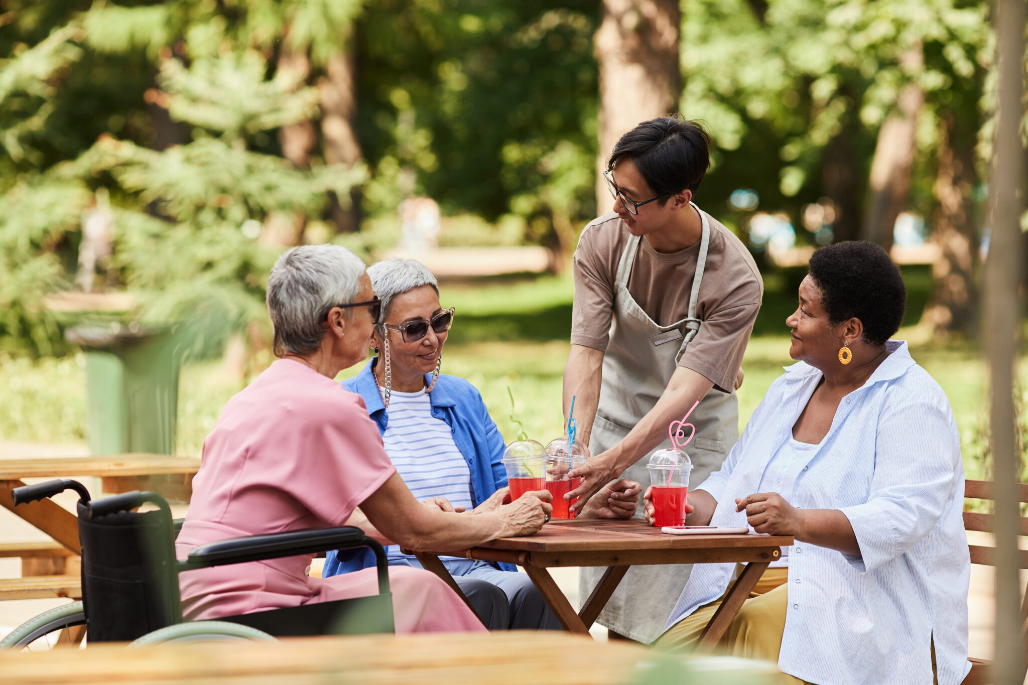 Portrait of young Asian waiter serving drinks to group of senior women at outdoor cafe assisted living communities